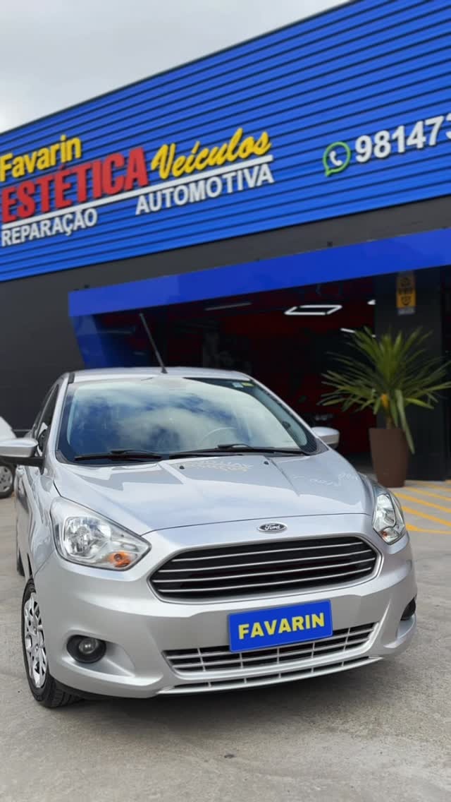 Carro prata posicionado em frente à oficina com a fachada ao fundo.