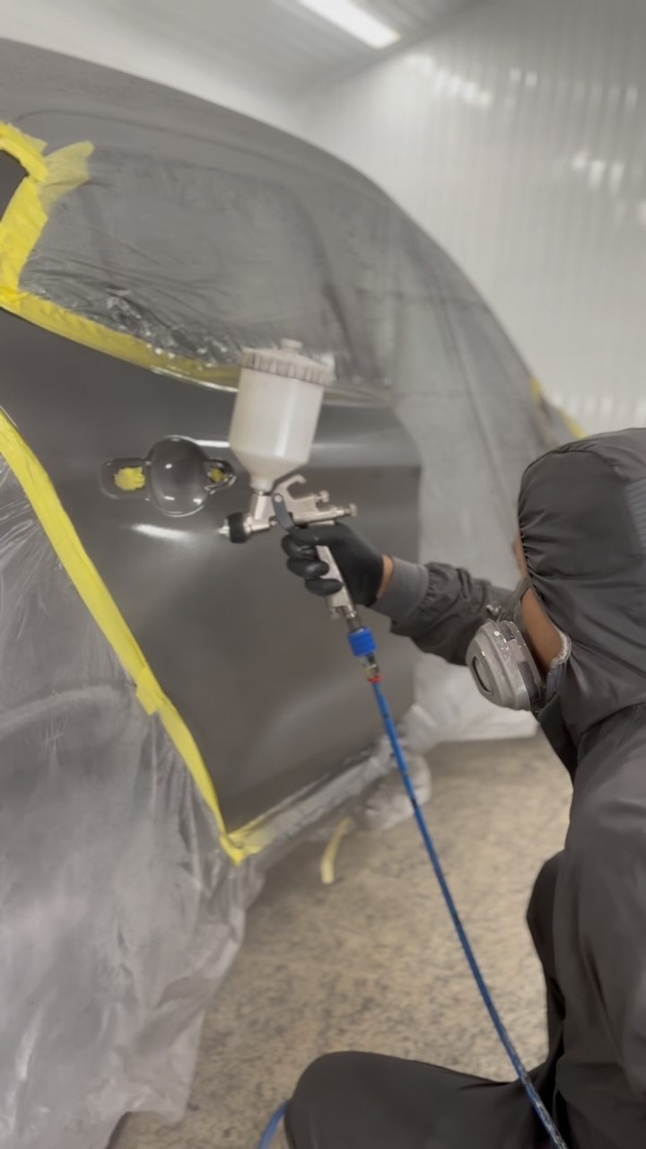 Profissional realizando pintura automotiva com pistola em cabine preparada.